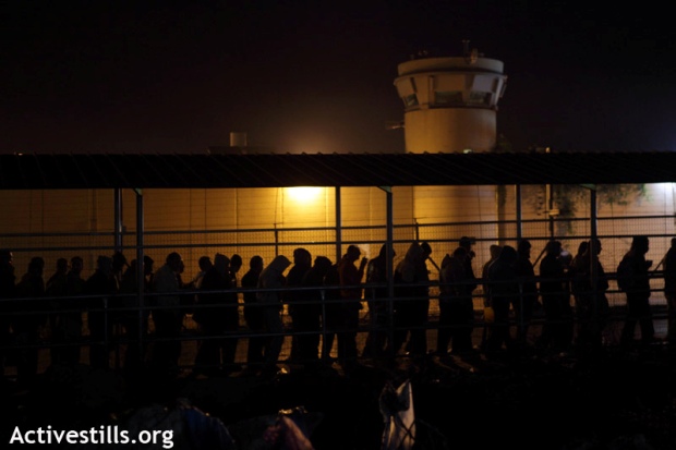 Palestinians workers walk in the early morning next to the Wall and an Israeli military tower to cross the Eyal Israeli military checkpoint, November 2011 (photo: Activestills)
