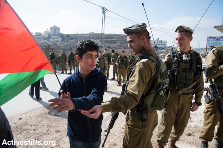 A Palestinian boy slaps aside a piece of candy offered by an Israeli soldier during the weekly demonstration against the Israeli separation barrier in the West Bank village of Al Ma'sara, January 17, 2014. The separation barrier would cut off the village from its agricultural lands if it is built as planned. (photo: Ryan Rodrick Beiler/Activestills.org)