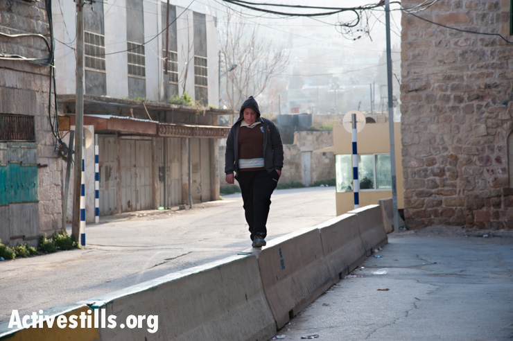 A Palestinian youth balances atop the concrete barrier segregating Israeli and Palestinian traffic on a section of Hebron's Shuhada Street. The barrier on this section of street has since been removed.