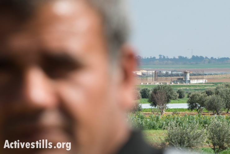 An Israeli military post is seen over the shoulder of a Palestinian farmer whose fields lie on Gaza's eastern border, Al Montar, February 17, 2014. (photo: Ryan Rodrick Beiler/Activestills.org)