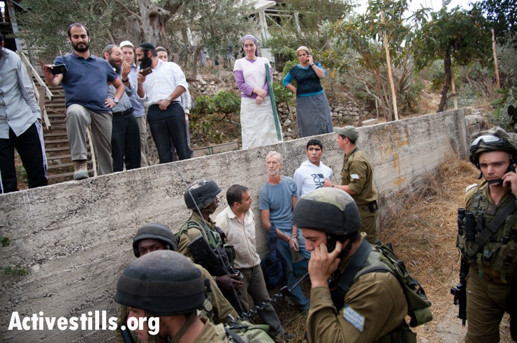 With Israelis from Tel Rumeida settlement looking on from above, Israeli soldiers arrest two Palestinians and an international volunteer after confrontations between settlers, the Al Azzeh family who had just harvested their olives, and the military, October 22, 2012. The arrests followed the first time the Al Azzeh family was able to harvest their olives since 2007. Despite Israeli court confirmation of Al Azzeh family's ownership of the grove, their harvest was disrupted by settlers, after which soldiers ordered the family to leave their trees.