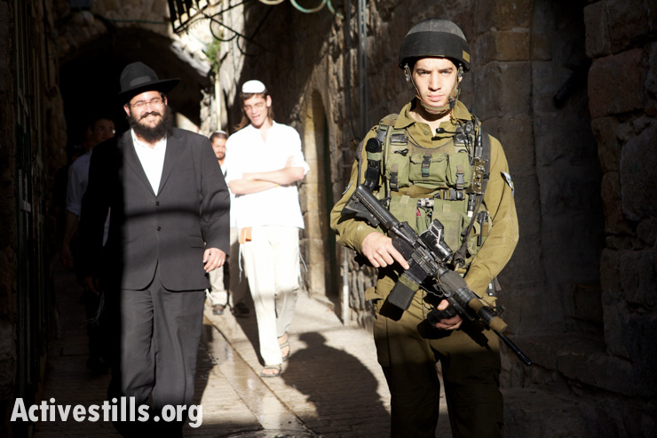 An Israeli soldier stands in the streets of the old city of Hebron next to a group of settlers, escorting them during their tour of the February 20, 2010. Settlers have started to tour the old city of Hebron every Saturday. In addition to a military escort, many of the settlers are armed. In the process, they disrupt the lives of Palestinians, often harassing them on the way. 