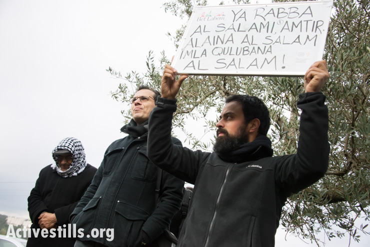 A Palestinian holds a board with song lyrics as International Christian activists attending the Christ at the Checkpoint conference join Palestinians for a Catholic mass in a West Bank olive grove as a form of nonviolent resistance against the Israeli separation barrier that threatens to further divide land belonging to the town of Beit Jala, March 14, 2014. The lyrics read, "Oh, God of peace, rain down peace on us. Oh God of peace, fill our hearts with peace." (photo: Ryan Rodrick Beiler/Activestills.org)