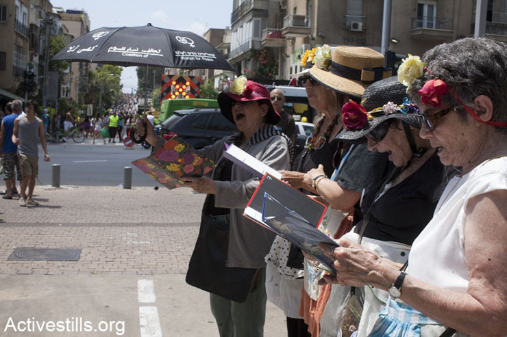 “The Angry Grandmothers” perform a song against the Israeli occupation during a protest vigil by the “Women in Black” in central Tel Aviv. In the background people are marching in the Tel Aviv Pride Parade, June 7, 2013.