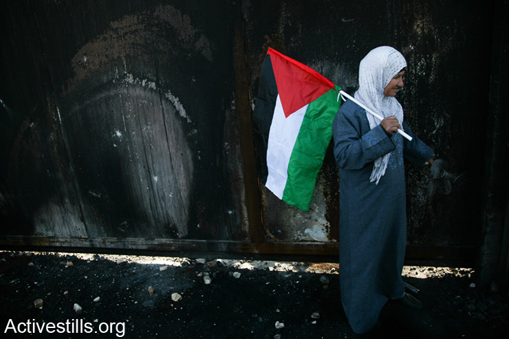 A Palestinian woman stands near a gate in the Israeli wall during a protest marking 9 years for the struggle against the wall in the West Bank village of Bilin, February 28, 2014. (photo: Hamde Abu Rahma/Activestills.org)