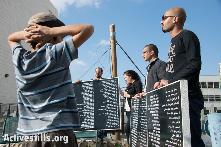 An Israeli child stops to watch  a procession of Israeli, Palestinian, and international activists carrying names of those who died in the Deir Yassin massacre, Givat Shaul, West Jerusalem, April 10, 2014. On April 9, 1948, some 100-200 Palestinians, including women and children, were killed by the extremist Zionist militias the Irgun and Stern Gang (Lehi) in the village of Deir Yassin. The Israeli activist group Zochrot ("remembering") organizes an annual procession to commemorate those killed and to recount the history of the village. (photo: Activestills.org)