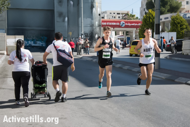 Race leaders Morten Hvidtfelet (black shirt) and Anders Roemer of Denmark cross paths with a Palestinian family taking a more leisurely pace near the Israeli separation wall dividing the West Bank town of Bethlehem in the second annual Palestine Marathon, April 11, 2014. Hvidtfelet and Roemer later won the race simultaneously in 2:51:13. (photo: Activestills.org)
