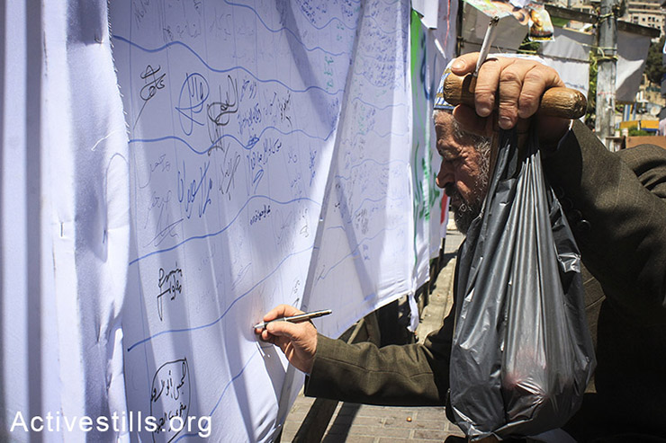 A Palestinian man signs a solidarity letter for the hunger-striking administrative prisoners hanged beside the protest tent in the city center of Nablus, West Bank, May 2nd, 2014. (Ahmad al-Bazz/Activestills.org
