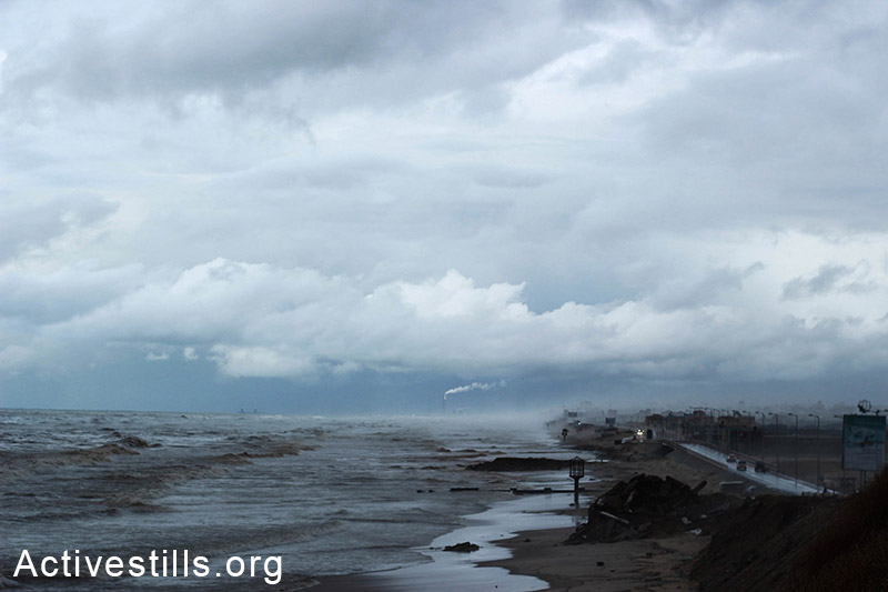 Clouds hang above the Gaza coast during a stormy day as smoke rises from a power plant across the border in Ashdod, Israel.  (Basel Yazouri/Activestills.org)