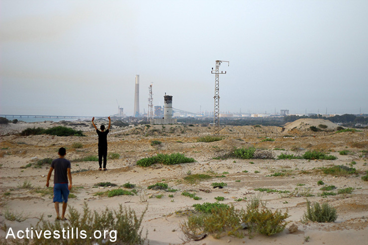 Young Palestinians wave at an Israeli military tower in the 'No-go zone' area, near the border close to the Palestinian village of As Siafa in north Gaza, May 30, 2014. The Israeli army classified broad swaths of land adjacent to the Green Line, in which soldiers are allowed to open fire at anybody who enters, even if the person poses no threat. In early 2010, the army disseminated leaflets in the Gaza Strip warning residents it is forbidden to go within 300 meters of the fence, and that all means, including gunfire, will be used against those who violate the prohibition. The lax rules of engagement in these areas endanger farmers and residents who live nearby.
