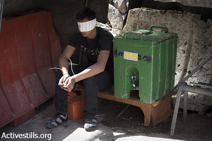 Palestinian youth sits blindfolded in a checkpoint after Israeli soldiers arrested him during clashes in the West Bank city of Hebron, June 16, 2014. (Oren Ziv/Activestills.org)
