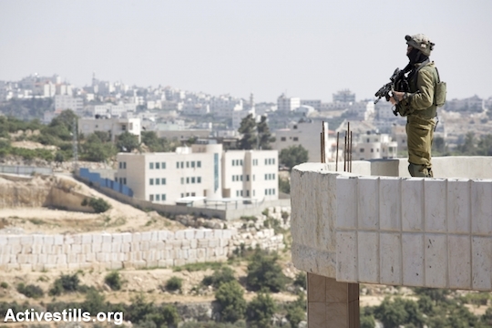 An Israeli soldier stands on the rooftop of a Palestinian home in the West Bank city of Hebron, June 18, 2014. (File photo by Oren Ziv/Activestills.org)