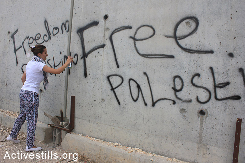 A Palestinian sprays slogans on the separation wall during the 'Return March' held near Tulkarem, West Bank, May 31, 2014. 