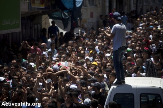 Mourners carry the body of killed Palestinian Mohammed al-Araj during his funeral at the Qalandiya Palestinian refugee camp near the West Bank city of Ramallah, on July 25, 2014, after he was shot and killed the night before during clashes with the Israeli army amid a massive protest in the West Bank against the Israeli attack on the Gaza strip. (photo: Activestills)