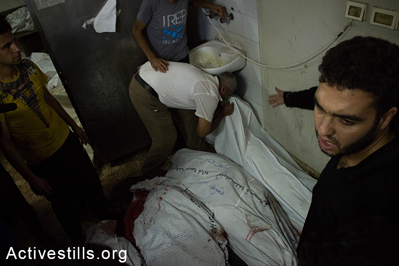 A relative kisses a body of a family member at the Al Shifa hospital as more bodies arrive from the Al-Shejaiya area, July 20, 2014. (Basel Yazouri/Activestills.org)