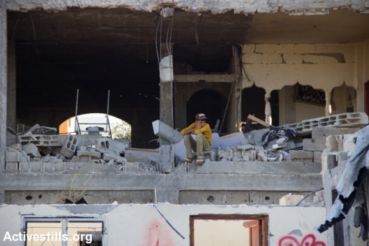 A Palestinian man retrieves his belongings from the rubble of a destroyed house in Beit Hanoun following bombardment by Israeli forces, northern Gaza Strip, August 11, 2014. According to OCHA, 16,800 homes in the Gaza Strip have been destroyed or severely damaged, leaving 370,000 displaced. (photo: Activestills)