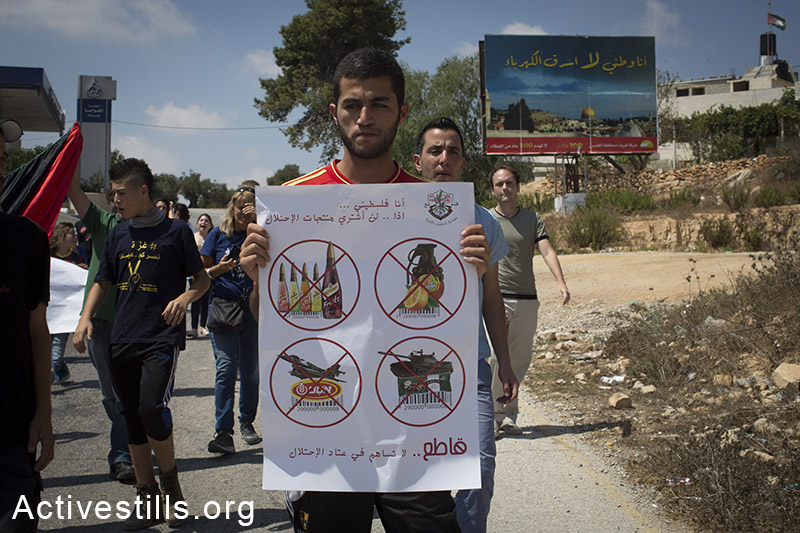A Palestinian youth holds a sign calling to boycott Israeli goods during the weekly protest against the Israeli occupation in the West Bank village of Nabi Saleh, August 22, 2014.(Activestills.org)