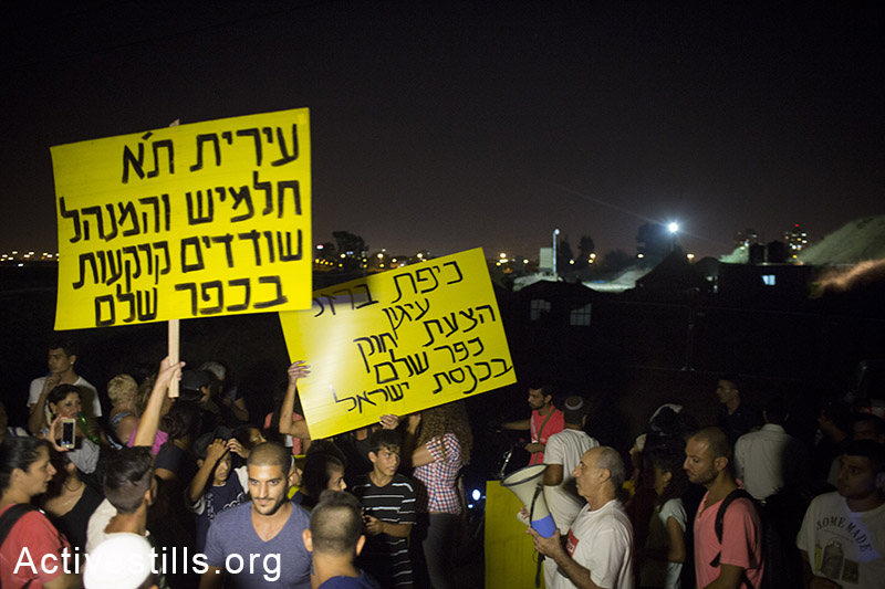 Residents of Kfar Shalom neighborhood in South Tel Aviv protest against the plan to evict houses in the neighborhood and calling for betterment of welfare services in Israel, next to the  'Iron Dome' battery, a missile defence system designed to intercept and destroy incoming rockets, in South Tel Aviv, August 24, 2014. (Activestills.org)