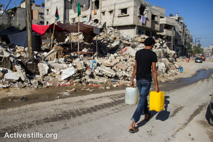 A Palestinian carries jugs of water through a destroyed section of the Shujayea neighborhood, east of Gaza city, September 4, 2014. (Activestills.org)