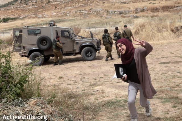 Woman arriving at the spring, passing soldiers (Anne Paq / Activestills)