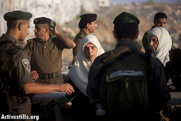 A Palestinian woman shows her ID to an Israeli border policeman, while Palestinian security forces stand in the background, as she crosses from the Qalandiya checkpoint on the first Friday of Ramadan, July 20, 2012. (photo: Oren Ziv/ Activestills.org)