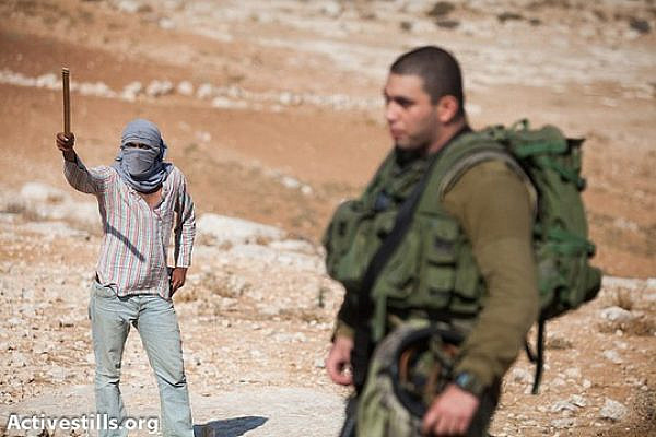 Protected by an Israeli soldier, a masked settler threatens activists with a stick in front of Ma´on settlement during a solidarity march in the South Hebron Hills, September 22, 2012. (photo: Activestills.org)
