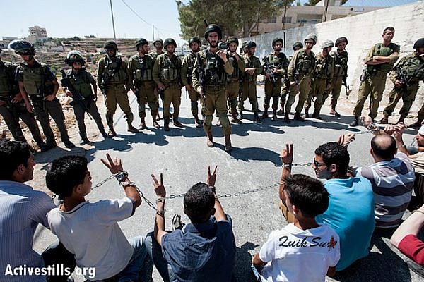 Palestinian activists wrapped in chains in solidarity with prisoners in Israeli jails confront heavily armed Israeli soldiers during a weekly nonviolent demonstration against the separation wall, Al Ma'sara, West Bank, September 14, 2012. If completed as planned, the barrier will cut off the village from agricultural lands owned by its residents. The previous day also marked 19th anniversary of the Oslo interim peace accords, renewing calls for the release of prisoners jailed before the agreement was signed. (photo: Ryan Rodrick Beiler/Activestills.org)