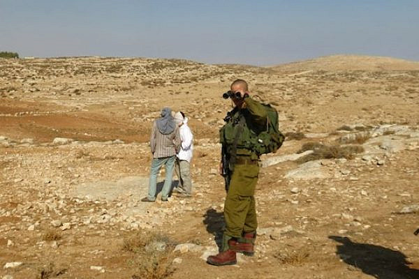 IDF soldier turns a blind eye to violent settlers from Havat Maon (photo: Israeli Ta'ayush activist)