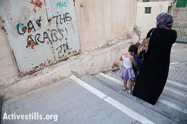 A Palestinian woman and children pass the slogan "Gas the Arabs! JDL" spray-painted on an exterior wall of the Cordoba School near Shuhada Street, Hebron, October 22, 2012. "JDL" stands for Jewish Defense League, an extremist group founded by Meir Kahane and designated as a terrorist group by the FBI. On February 25, 1994, JDL charter member Baruch Goldstein opened fire on Muslims at Hebron's Al-Ibrahimi Mosque (Cave of the Patriarchs), killing 29 worshippers and injuring 125. Afterwards, the JDL designated him "a martyr in Judaism's protracted struggle against Arab terrorism." (photo by: Ryan Rodrick Beiler/Activestills.org)