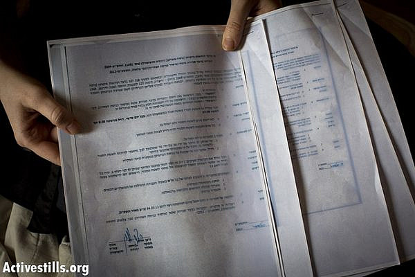 An Israeli activist shows documents given to her by Israeli policemen, arriving to her house at 6 a.m., as she sits in her house in Tel Aviv, November 11, 2012. (photo: Activestills)