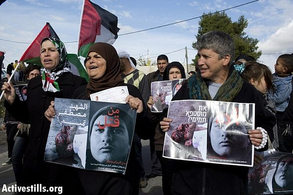 Palestinian and Israeli activists hold a poster asking "Who Killed Mustafa Tamimi?" during the weekly protest against the occupation in the West Bank village of Nabi Saleh, December 7, 2012. Tamimi was killed on December 9, 2011, when he was shot in the face with a tear gas canister at close range by Israeli soldiers. Also pictured on the poster is soldier who killed Tamimi. No one responsible for Tamimi's death has been brought to justice to this day. (photo by: Oren Ziv/ Activestills.org)