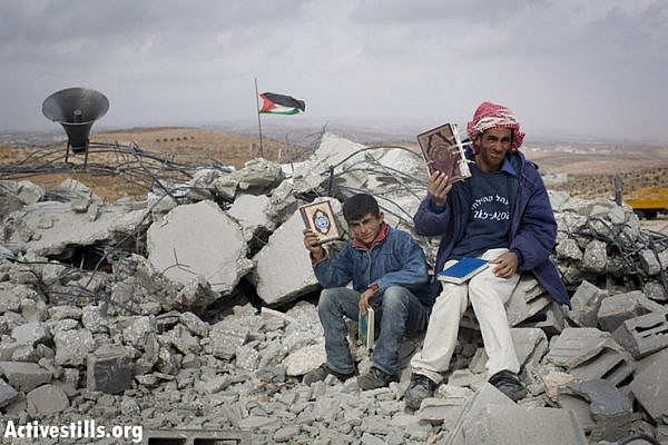 Fadel hammadi and his son, Abed, hold copies of the Koran as they sit on top of a mosque that was demolished by Israeli forces in the West Bank village of al-Mufaqara, south of Hebron, on December 4, 2012. (photo by: Oren Ziv/ Activestills.org)