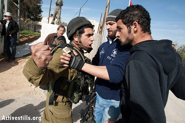 An Israeli soldier threatens to punch a Palestinian activist during a weekly nonviolent demonstration against the Israeli separation barrier, Al Ma'sara, West Bank, January 18, 2013. If completed as planned, the wall would cut off the village from its agricultural lands. (Photo by: Ryan Rodrick Beiler/Activestills.org)