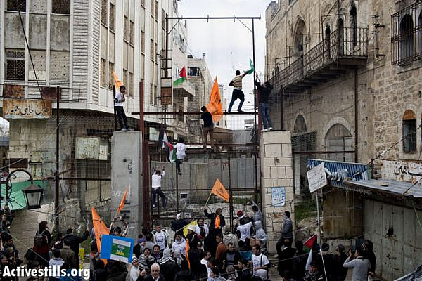 Demonstrators climb on a fence, built by the Israeli army to close Shuhada Street to Palestinians, in the West Bank city of Hebron February 22, 2013. (Photo by: Oren Ziv/Activestills.org)