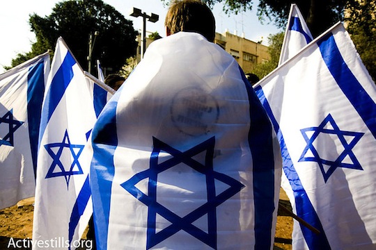 A right wing protester holds up Israeli flags while thousands march in the annual human rights march in Tel Aviv. Photo by Activestills.org