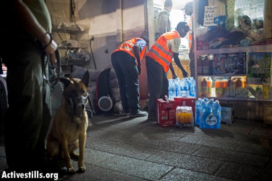 Policeman and attack dog watch over African workers emptying asylum seeker's store (Oren Ziv / Activestills)