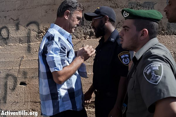 A Palestinian man stands in front of Israeli border policemen next to an outer wall of his house that had a graffiti writing sprayed on it, reading: "We will not remain silent over stone throwing" (loose translation). The price tag action in which two Palestinian-owned houses were spray painted and at least 20 cars were vandalized took place in the Palestinian neighborhood of Beit Hanina in East Jerusalem, June 24, 2013. (Photo by guest photographer: Tali Mayer/Activestills.org)