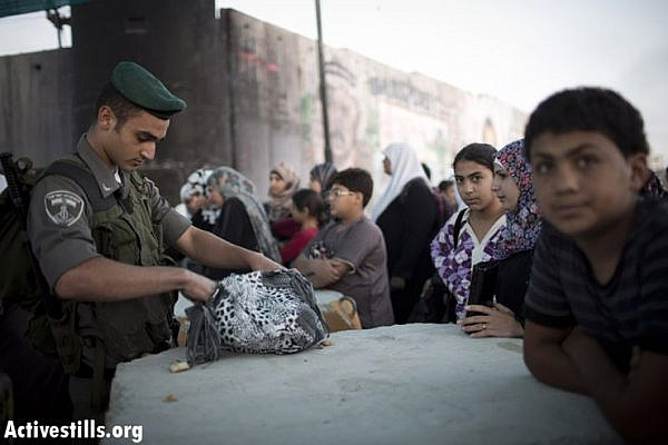 A Israeli border policeman check the bag of a Palestinian woman as she wait to cross from Qalandiya checkpoint outside Ramallah, West Bank, into Jerusalem to attend the Ramadan Friday Prayer in the Al-Aqsa Mosque, July 26, 2013.
Photo by: Oren Ziv/Activestills.org