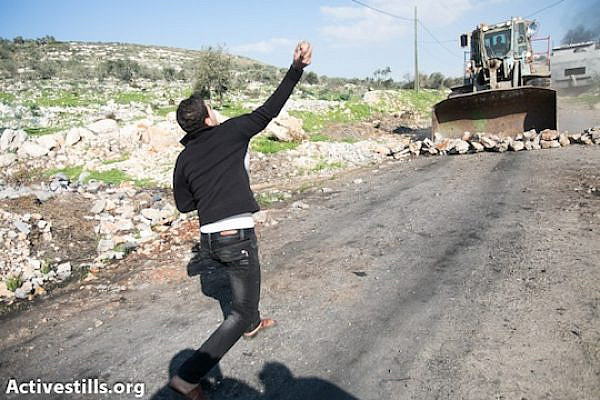 A Palestinian youth throws stones at an Israeli army bulldozer in Kufr Qaddum, December 28, 2012 (Yotam Ronen/Activestills.org)
