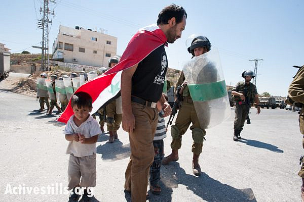 Palestinian activist Mohammad Brijiah and his twin 3-year-old sons confront Israeli forces blocking the road from their West Bank village of Al Ma'sara during a weekly demonstration against the separation barrier, September 6, 2013. If built as planned, the wall would cut off the village from its agricultural lands.