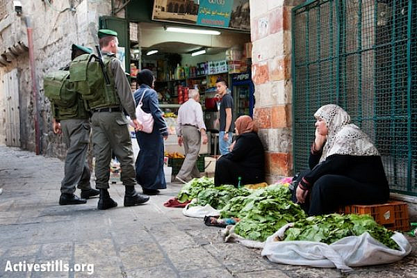 Israeli border police patrol near Palestinian women selling vegetables in the Old City near Damascus Gate, East Jerusalem, May 19, 2013. (Ryan Rodrick Beiler/Activestills.org)