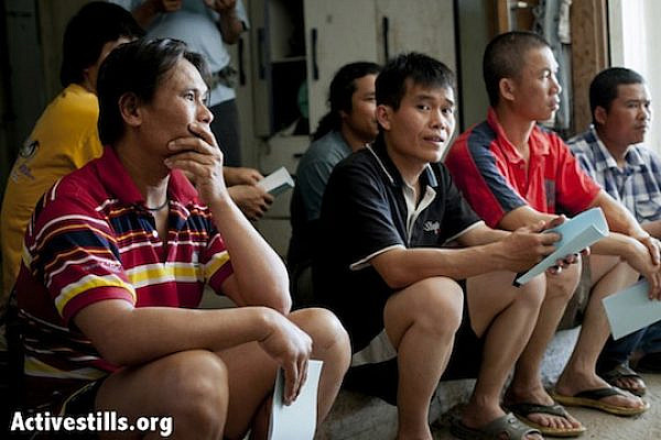 Thai workers sitting and listening at their residence in Kfar Varborg. (Shiraz Grinbaum/Activestills.org)
