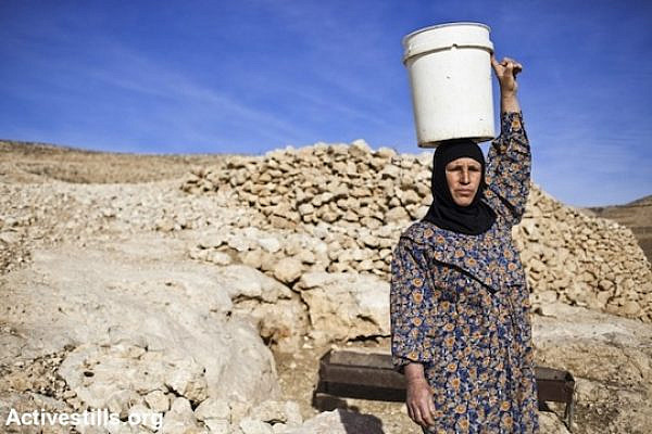 A Palestinian woman carries a bucket of water. (photo: Activestills)