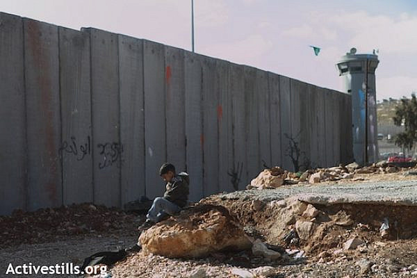 A Palestinian child sitting in front of a section of the Separation Wall in the refugee camp of Shuafat, East Jerusalem, December 27, 2011. (Photo: Anne Paq/Activestills.org)
