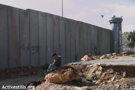 A Palestinian child sitting in front of a section of the Separation Wall in the refugee camp of Shuafat, East Jerusalem, December 27, 2011. (Photo: Anne Paq/Activestills.org)