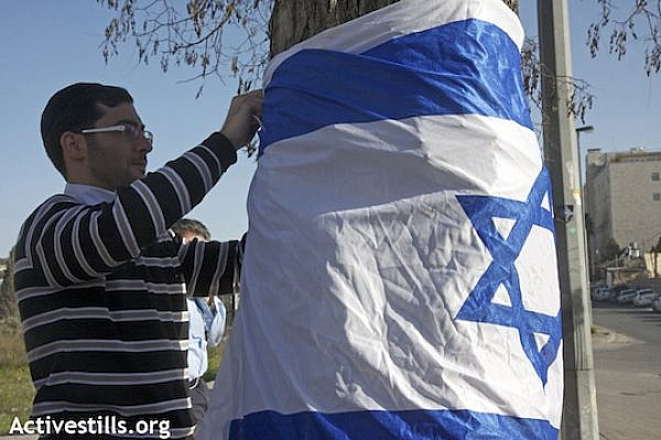 A Jewish settler attaches an Israeli flag to a tree in the East Jerusalem neighborhood of Sheikh Jarrah, January 29, 2010 (Anne Paq/Activestills.org)