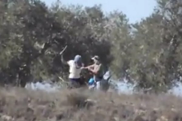 A mask settler strikes a Palestinian olive picker with a metal pole near the West Bank village of Burin. (Screenshot: Monir Kados/Yesh Din)