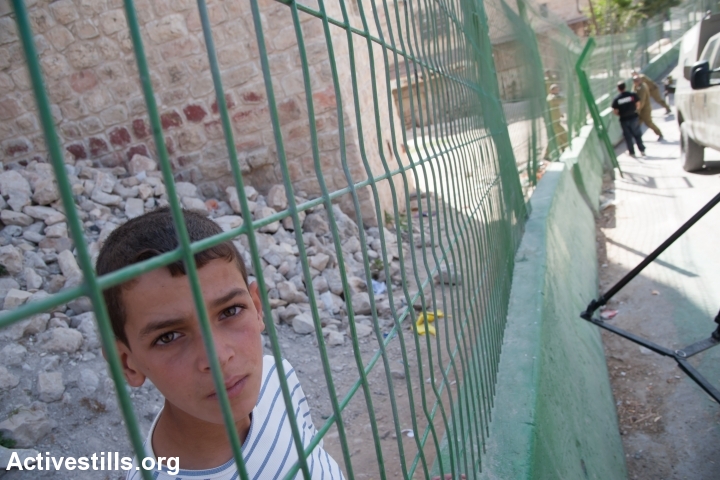 A Palestinian child watches as Israeli soldiers place a concrete and steel barrier to segregate Palestinian pedestrians from Israeli traffic along a road in the H2 section of Hebron, October 22, 2013. The road connects the Ibrahimi Mosque (Tomb of the Patriarchs) in Hebron's old city with the nearby Israeli settlement Kiryat Arba. Israelis are allowed to drive on the road, but Palestinians are prohibited from driving there without special permission. All settlements in the occupied Paletinian territories are illegal under international law. (photo: Ryan Rodrick Beiler/Activestills.org)