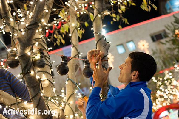 A Bethlehem-area activist hangs U.S.-made tear gas grenades used by the Israeli military in nearby Aida Refugee Camp on trees decorated for Christmas in Bethlehem's Manger Square, West Bank, December 2, 2013. (photo: Ryan Rodrick Beiler/Activestills.org)