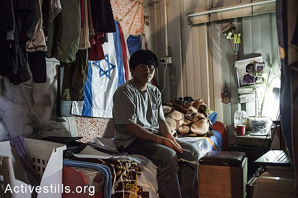 A Thai agricultural worker, sitting on his bed inside a shipping container, used as the group's residency, Moshav Yavetz, January 25, 2014. (Shiraz Grinbaum/Activestills.org)